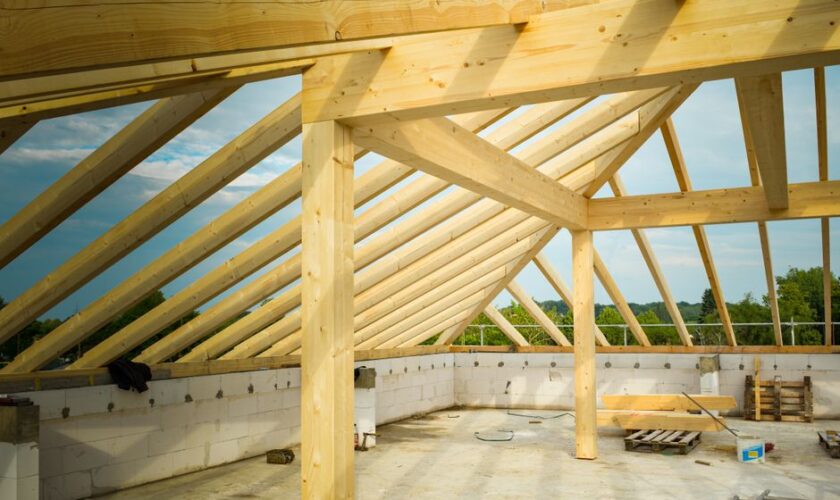 Unfinished construction site with a focus on wooden roof trusses under a clear sky.