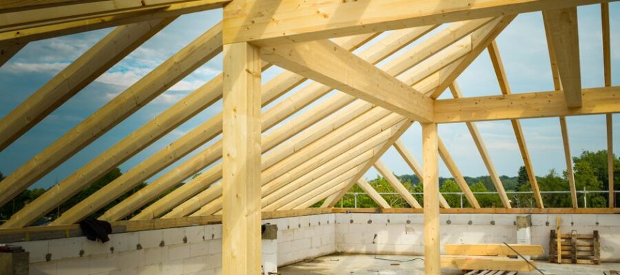 Unfinished construction site with a focus on wooden roof trusses under a clear sky.