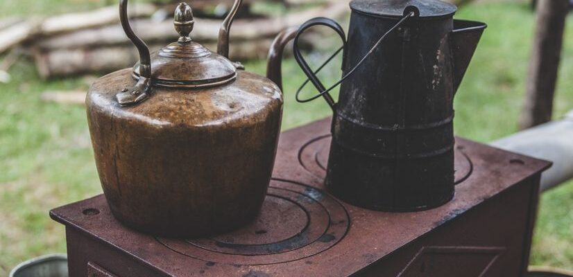 Vintage metal kettles on a rustic outdoor wood stove, creating a nostalgic rural scene.