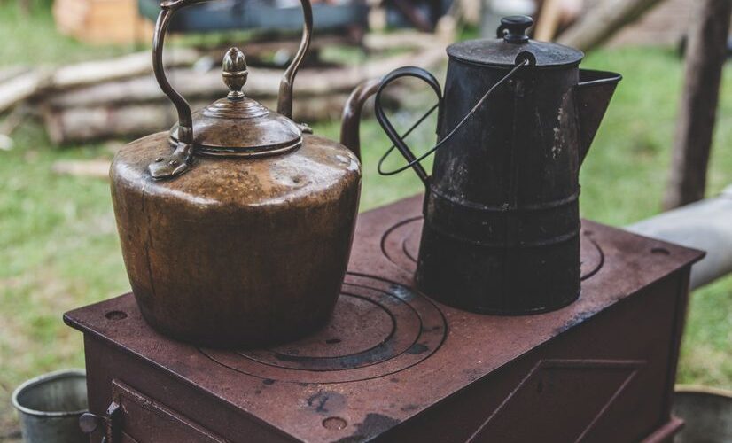 Vintage metal kettles on a rustic outdoor wood stove, creating a nostalgic rural scene.