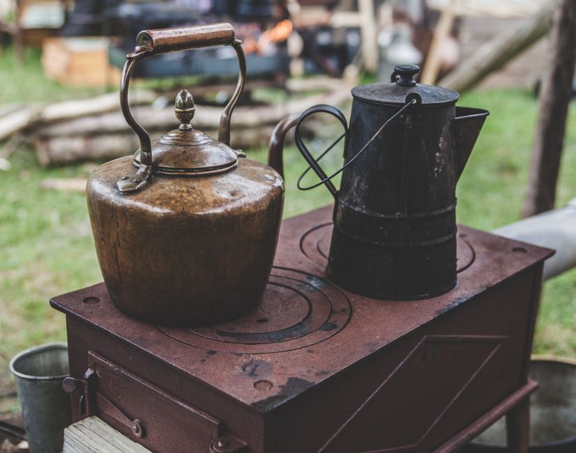 Vintage metal kettles on a rustic outdoor wood stove, creating a nostalgic rural scene.