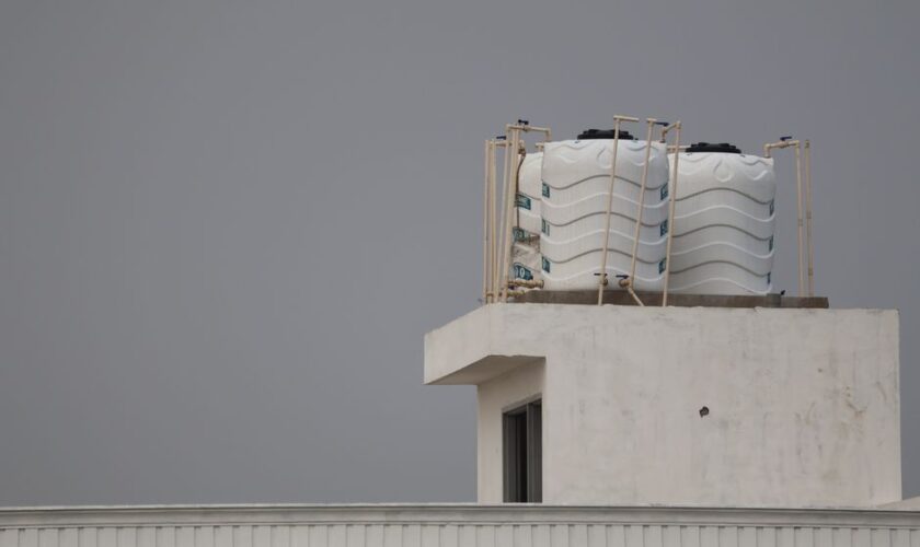 White water tanks on a rooftop with architectural design, under a gray sky.