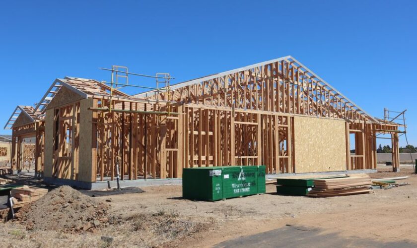 Wooden house frame construction under clear blue sky, sunny day.