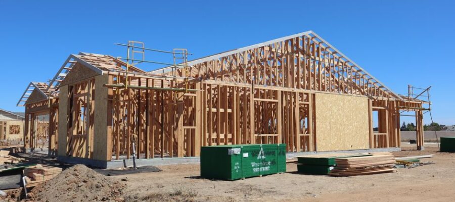 Wooden house frame construction under clear blue sky, sunny day.