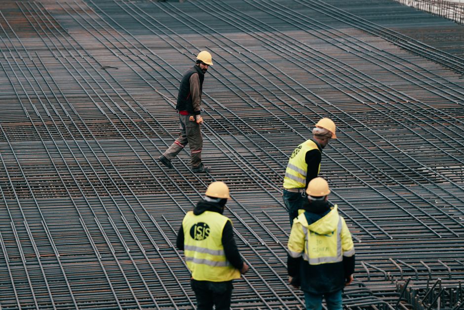 Workers in safety gear at a construction site with a focus on rebar grids.