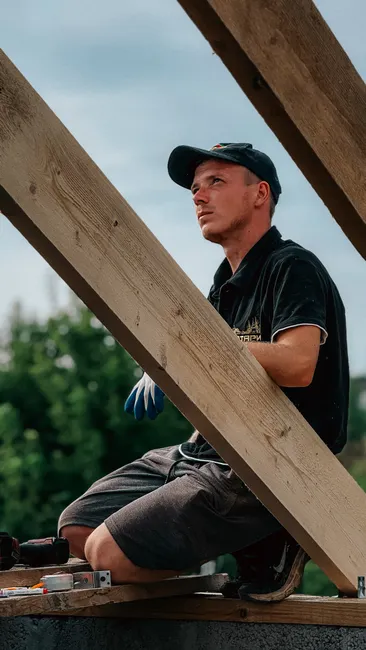 Young carpenter skillfully constructing a wooden roof framework outdoors.